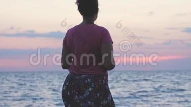 年轻女子站在岩石海滩上，在日落时缓慢地享受大自然。 3840x2160